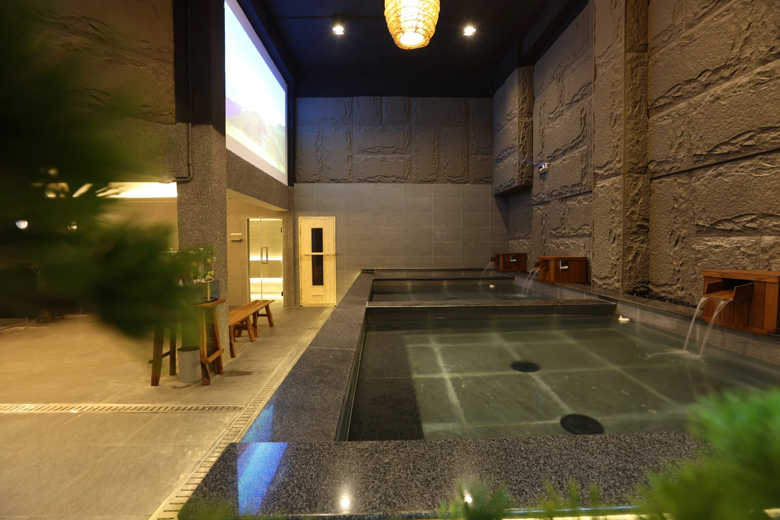 The full bath hall at Maxwell Onsen Bangkok — three mineral pools beneath a projection cinema wall