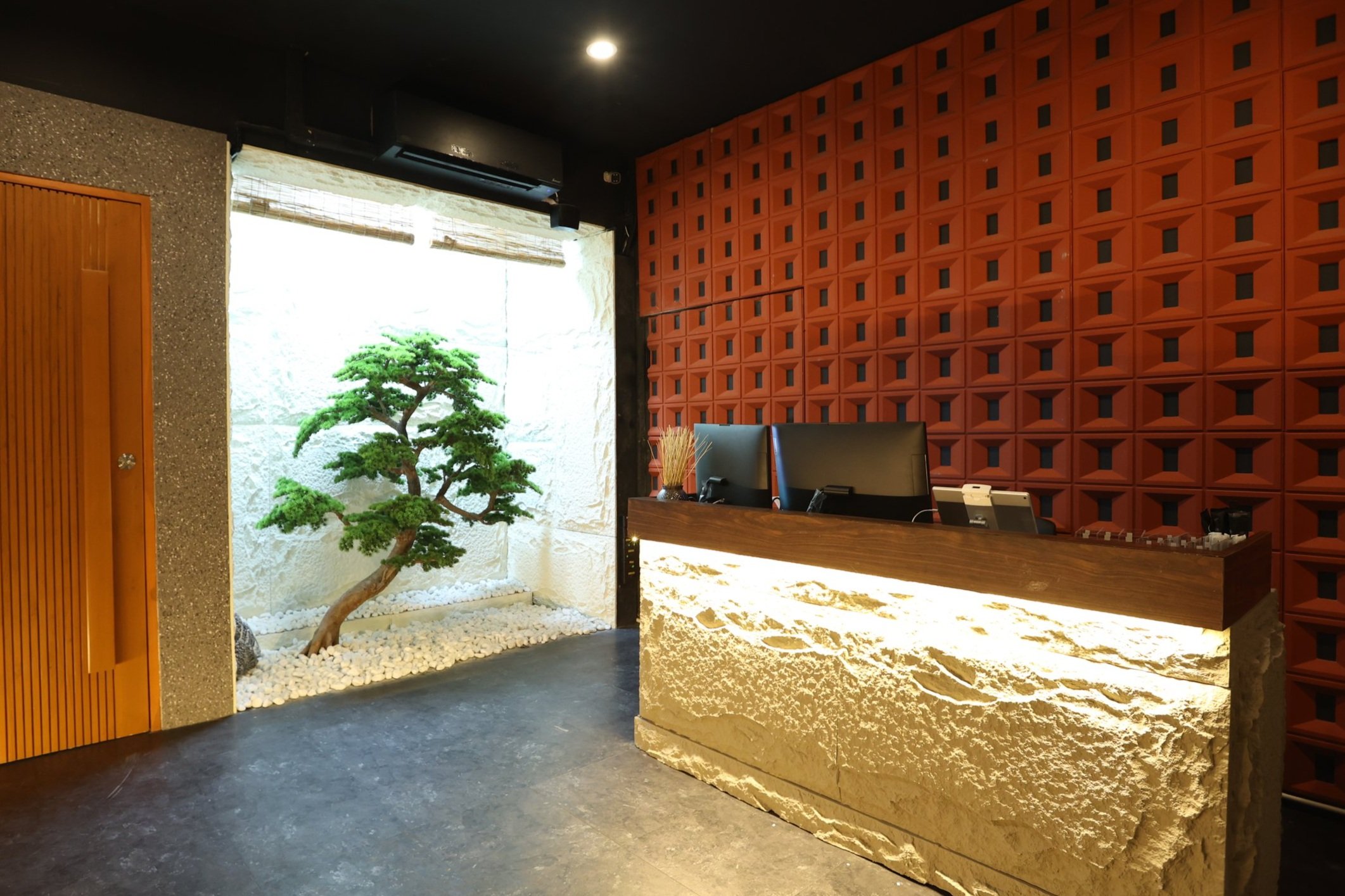Reception of Maxwell Onsen Bangkok with stone desk and bonsai courtyard